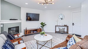 A living room with a fireplace, a round coffee table, sofas, a TV, and a ceiling light fixture.