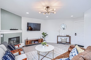 A living room with a fireplace, a round coffee table, sofas, a TV, and a ceiling light fixture.