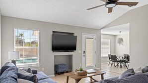 Ein modernes Wohnzimmer mit einem Flachbildfernseher, grauen Sofas, einem Holztisch und einem Deckenventilator.