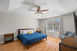 Een slaapkamer met een houten bed, een plafondventilator, een raam met gordijnen en een houten dressoir.