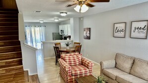 Una sala de estar con una escalera de madera, un sofá, un sillón estampado y un ventilador de techo.