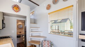 A compact kitchen with a built-in stove, wooden shelves, and a window with blinds. - Zion-Day-Trip Ready • Tiny Home + Mountain Views (Apple Valley)