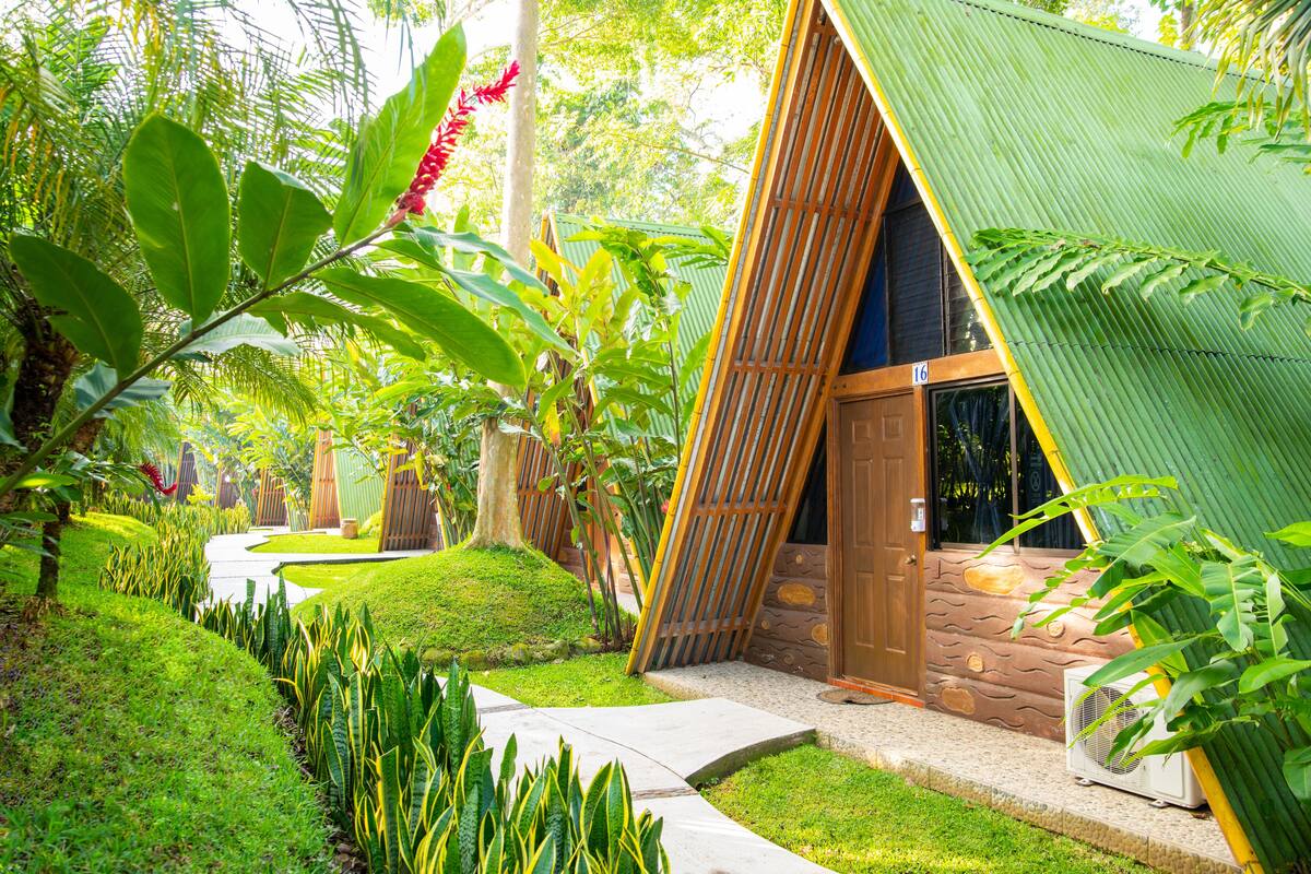 Un edificio de estilo tropical con techo inclinado, puerta de madera y un pequeño equipo de aire acondicionado.
