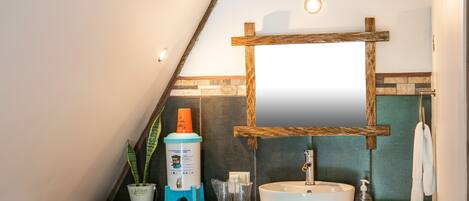 A bathroom with a wooden vanity, a white sink, a mirror, a towel rack, and a potted plant.