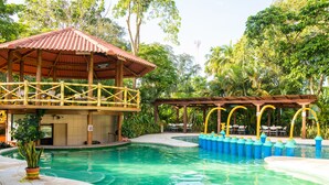 Un espace piscine agrémenté d’un pavillon en bois, d’un coin salon couvert et d’une piscine équipée de bouées de sécurité bleues.