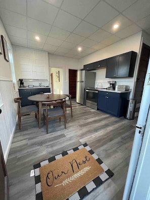 A modern kitchen with a dining area, featuring a central island, dark cabinetry, and a stainless steel refrigerator. - Cozy Lancaster Apartment Near Attractions (Lancaster)