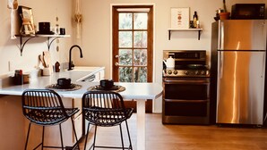 A kitchen with a stainless steel refrigerator, a double oven, a sink, and two black chairs at a small island.