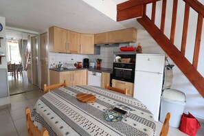 A compact kitchen with wooden cabinets, a dining table with a patterned tablecloth, and a white refrigerator.
