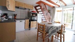Une cuisine avec des meubles en bois, une table à manger avec des chaises et un escalier menant à l’étage supérieur.