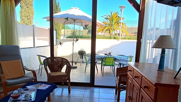 Une pièce comprenant un coin repas, une table recouverte d’une nappe bleue, des chaises en osier et un buffet.