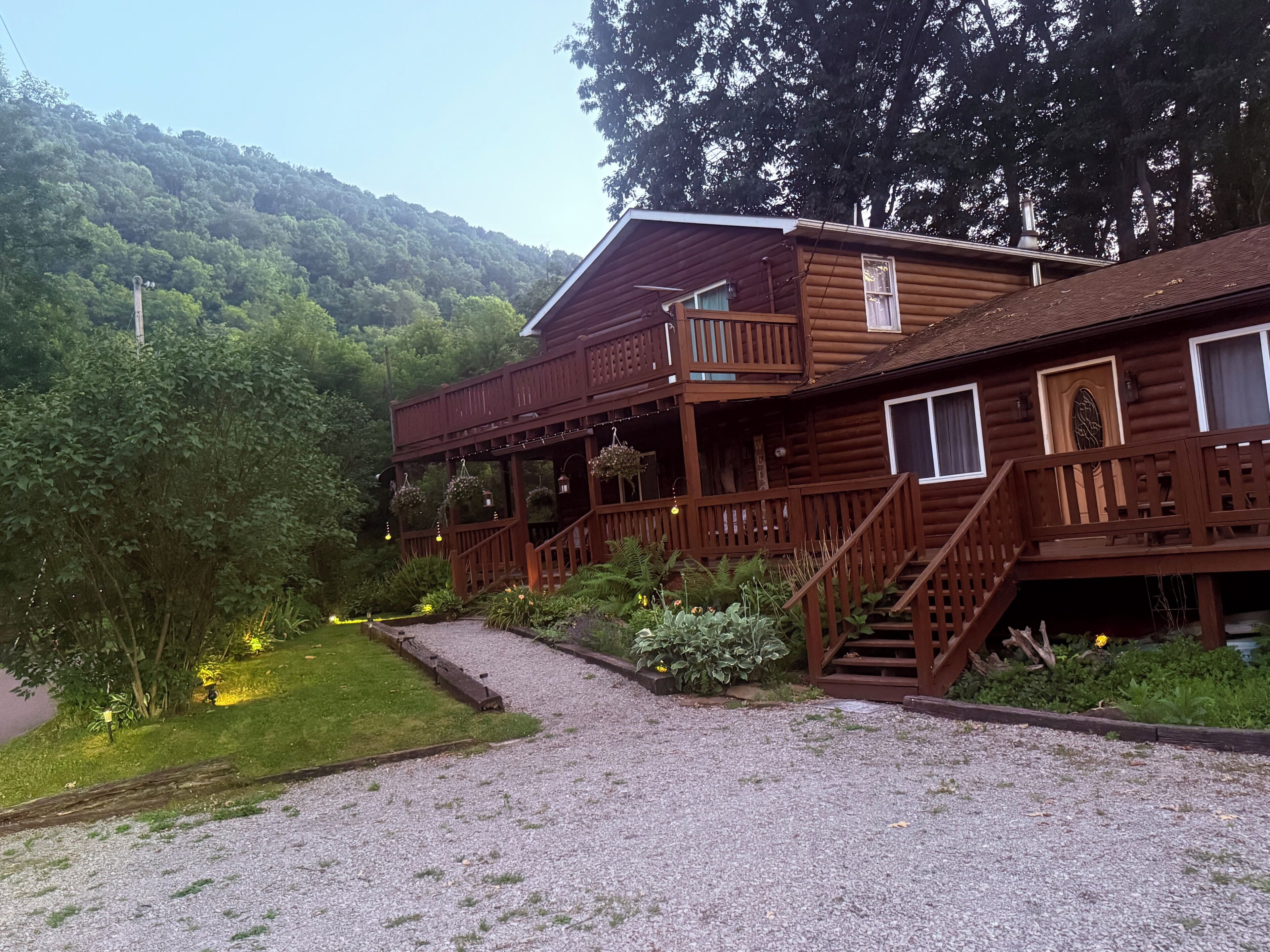 A wooden cabin with a balcony, a staircase, and a gravel path leading to the entrance.