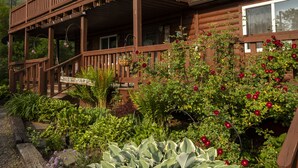 A wooden cabin with a porch, surrounded by lush greenery and flowering plants. - Casselman Cabin Retreat (Confluence)
