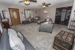 A living room with a grey sofa, armchairs, a wooden chest, and ceiling fans.