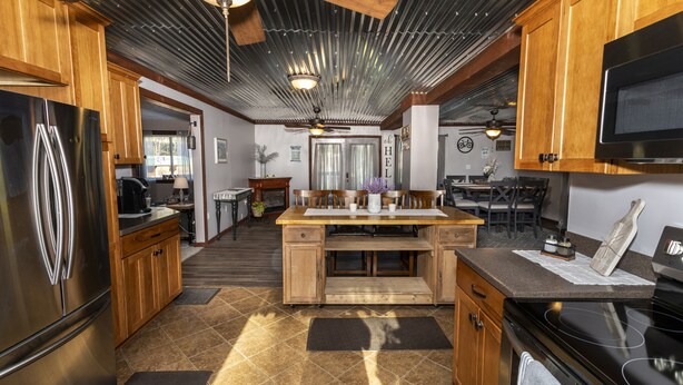 A modern kitchen with wooden cabinets, a stainless steel refrigerator, a black stove, and a central island with a sink. - Casselman Cabin Retreat (Confluence)
