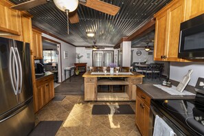 A modern kitchen with wooden cabinets, a stainless steel refrigerator, a black stove, and a central island with a sink.