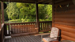 A wooden deck with a swing, a chair, and a table. - Casselman Cabin Retreat (Confluence)