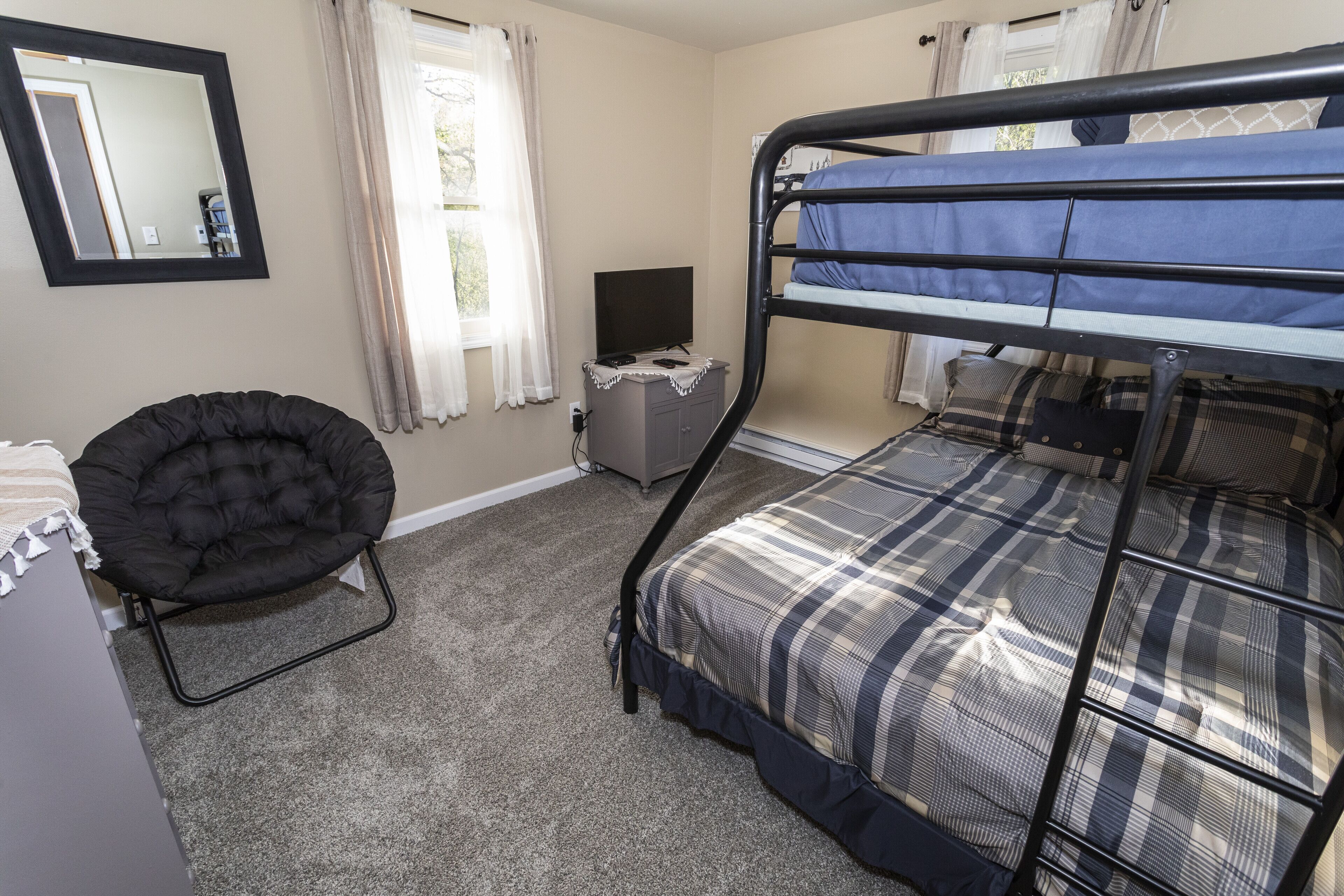 A room with a bunk bed, a chair, a desk, a television, and a mirror.