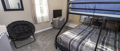 A room with a bunk bed, a chair, a desk, a television, and a mirror.