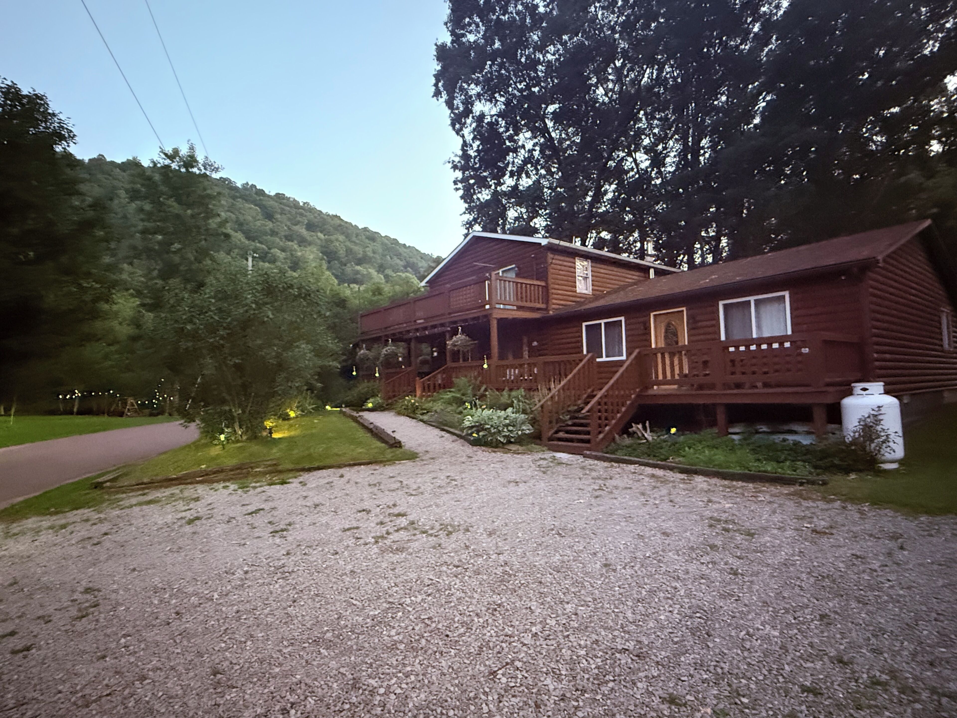 Une cabane en rondins à deux étages, avec une allée en gravier et une terrasse en bois.