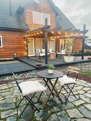 Une maison en bois dotée d’un patio couvert, aménagé avec du mobilier d’extérieur et des guirlandes lumineuses.