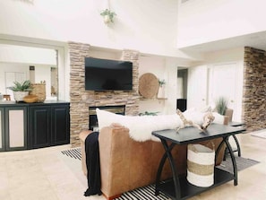A modern living room with a stone accent wall, a flat-screen TV, a brown leather sofa, and a black coffee table.