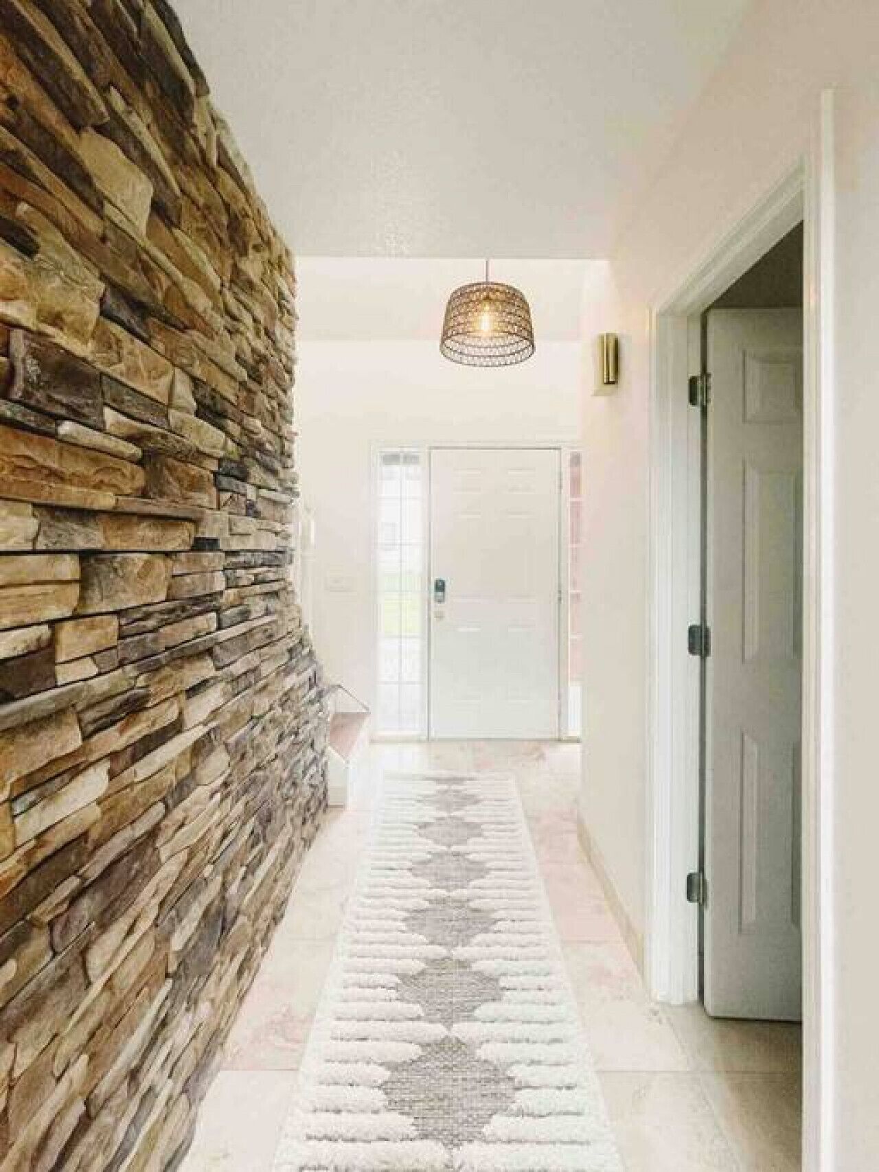 Un pasillo con pared de piedra, alfombra estampada y una puerta al final.