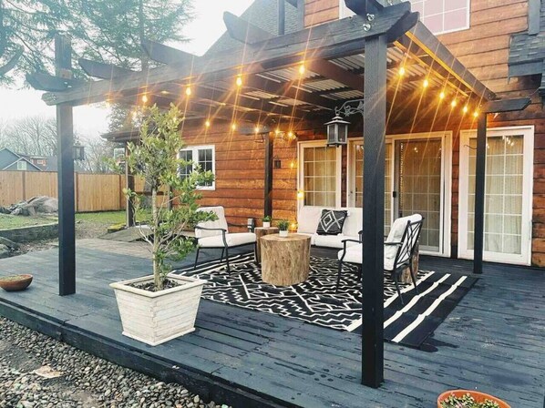 Une terrasse en bois avec des sièges d’extérieur, des guirlandes lumineuses et un pot de fleurs.