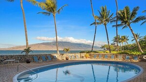 Une piscine avec des chaises longues et des palmiers, offrant une vue sur une plage et une montagne.