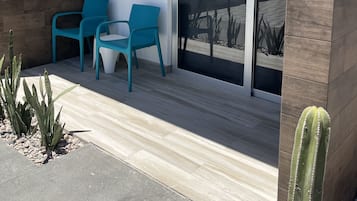 Uma área de pátio moderna com duas cadeiras turquesa e uma mesa, um painel de madeira e uma porta de vidro que dá para um jardim.