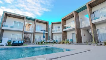 A modern hotel with a swimming pool, outdoor seating, and a clear blue sky.