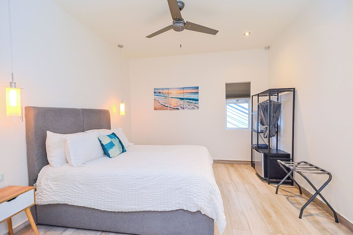 A bedroom with a bed, a ceiling fan, a wall-mounted TV, and a shelf with clothes.