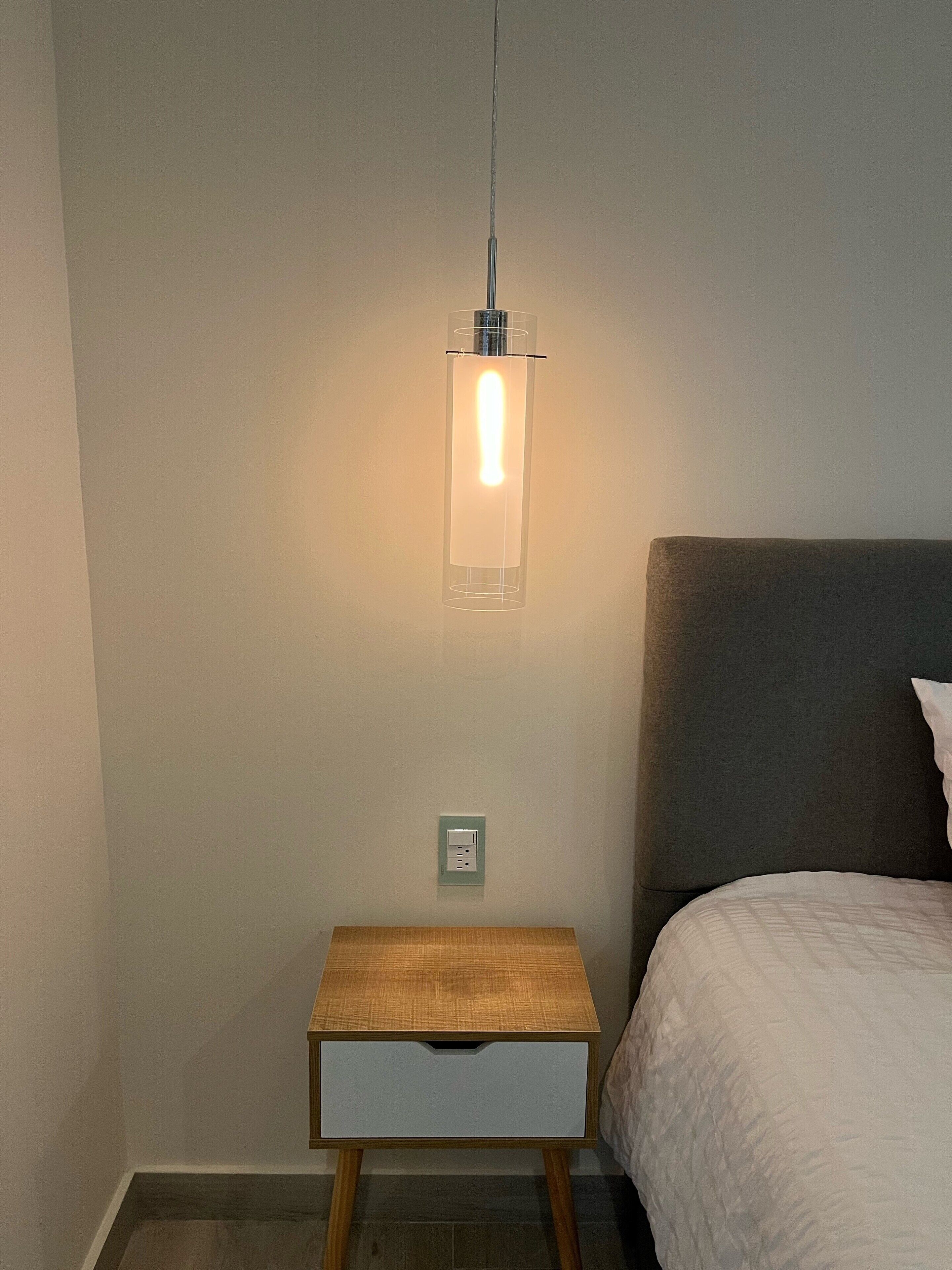 Un dormitorio con mesita de noche, cama, enchufe y lámpara colgante.