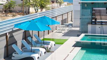 Relax by the ocean-view pool surrounded by lounge chairs and umbrellas, with a low wall and pebble edge.