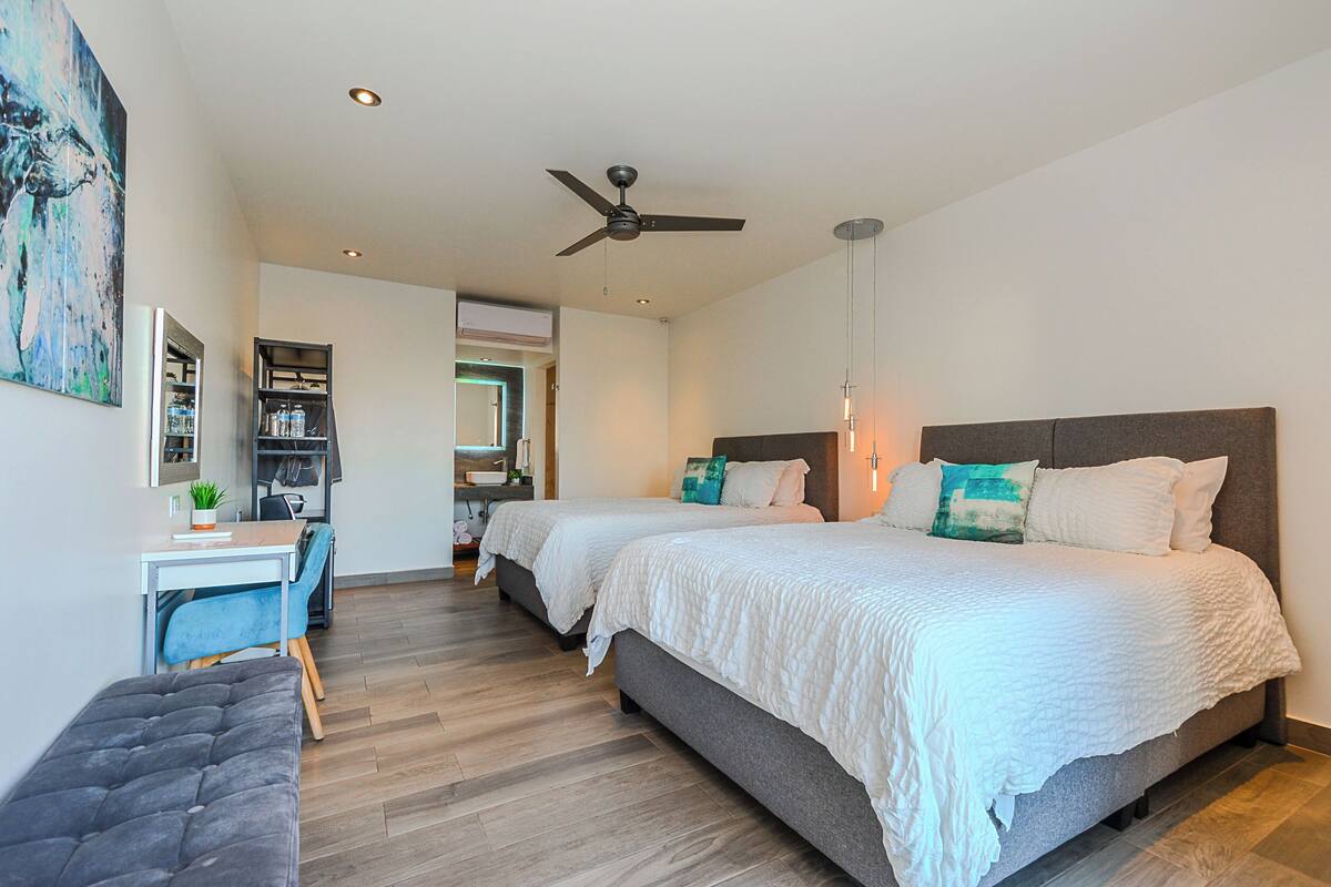 A modern bedroom with two beds, a desk, and a bench.
