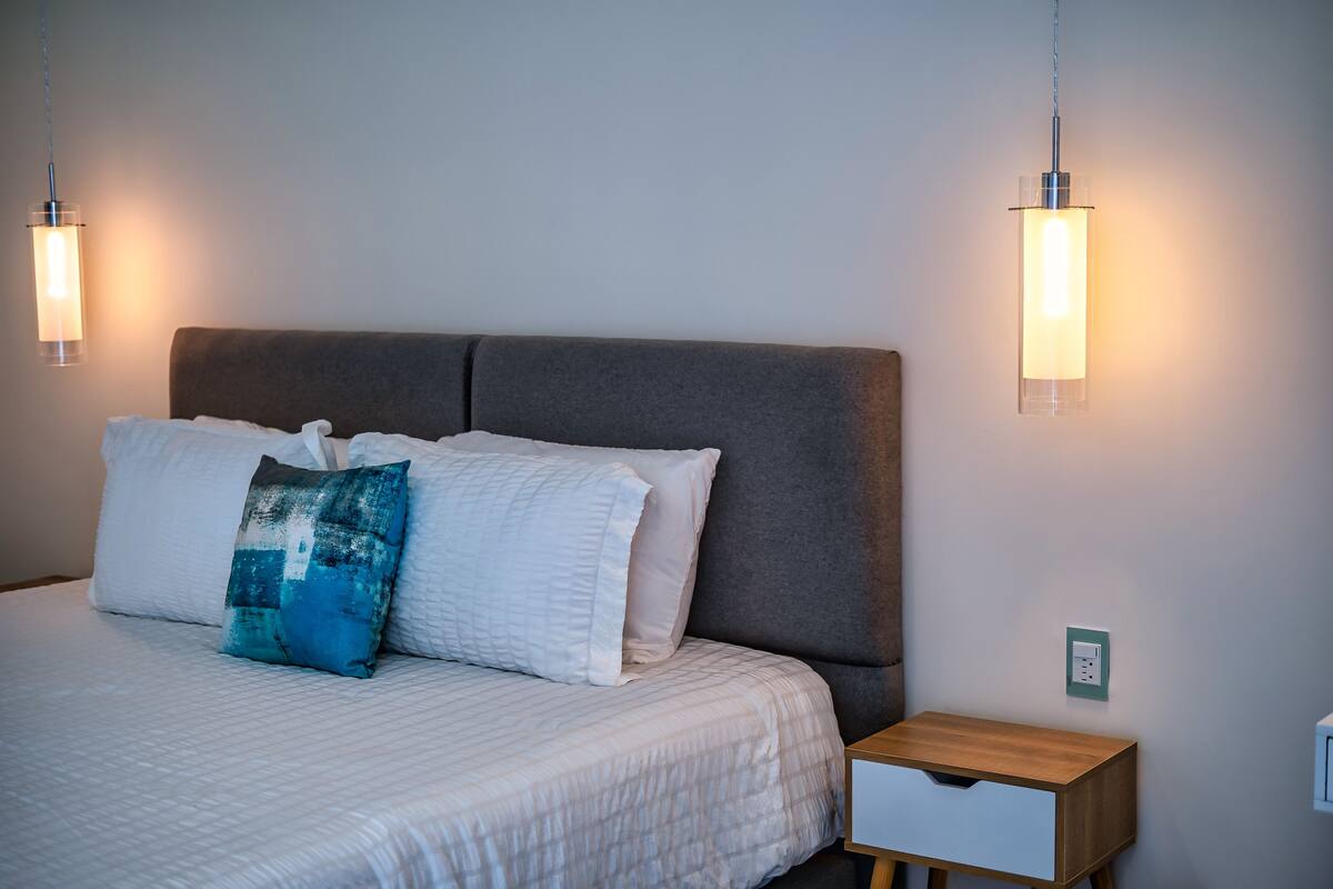 A neatly made bed with a grey headboard, two bedside lamps, and a small wooden nightstand.