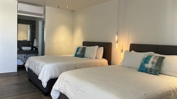 Ein Hotelzimmer mit zwei Betten, einem Deckenventilator, einem modernen Badezimmer mit großem Spiegel und einem integriertem Waschbecken.