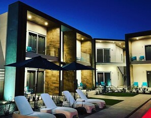 A modern multi-story building with lounge chairs and umbrellas outside. - The Cove Boutique Hotel Adults Only (Puerto Peñasco)