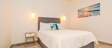 A bedroom with a bed, bedside table, and a wall-mounted painting.