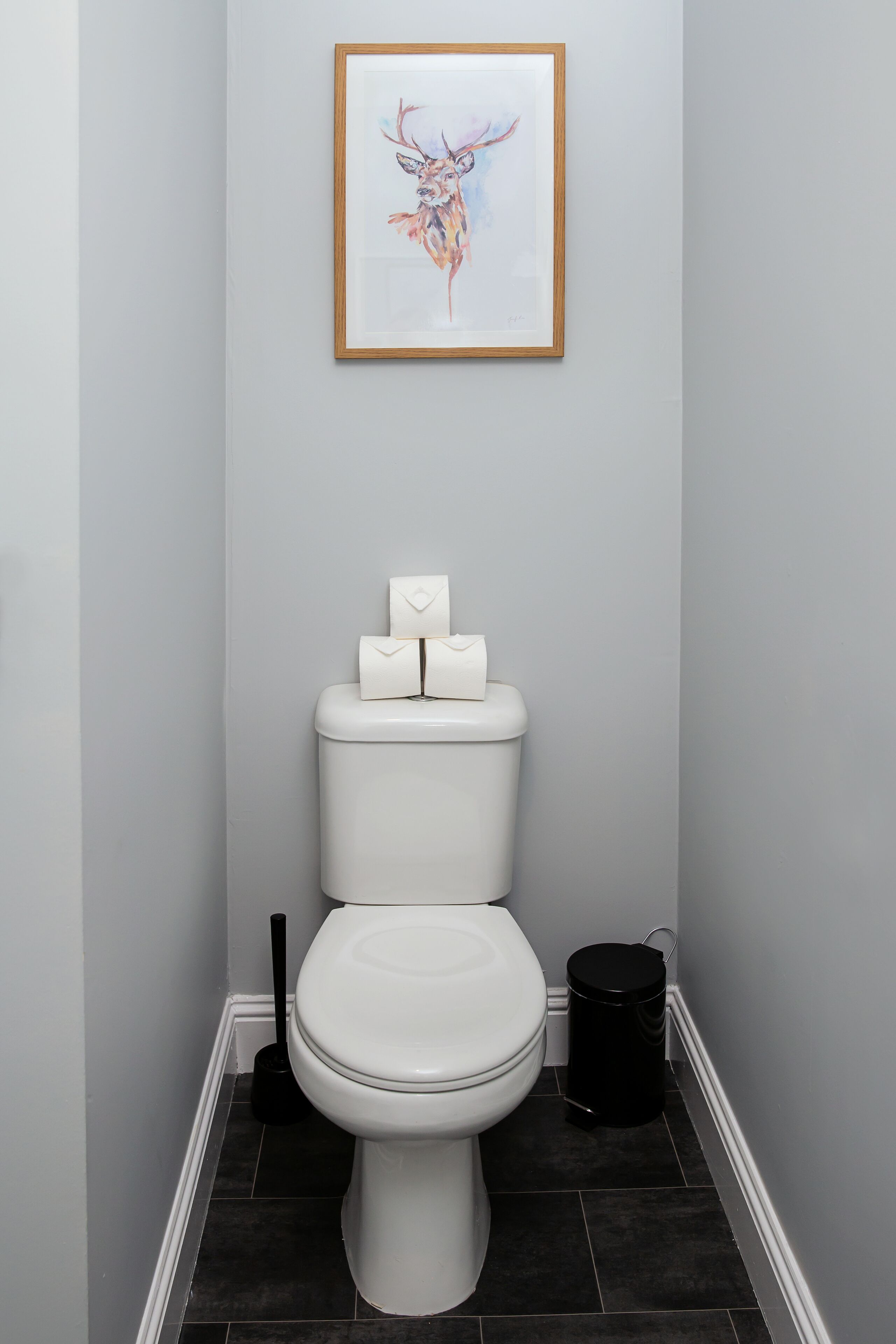 Ein Badezimmer mit einer weißen Toilette, einem schwarzen Mülleimer und einem gerahmten Kunstwerk an der Wand.