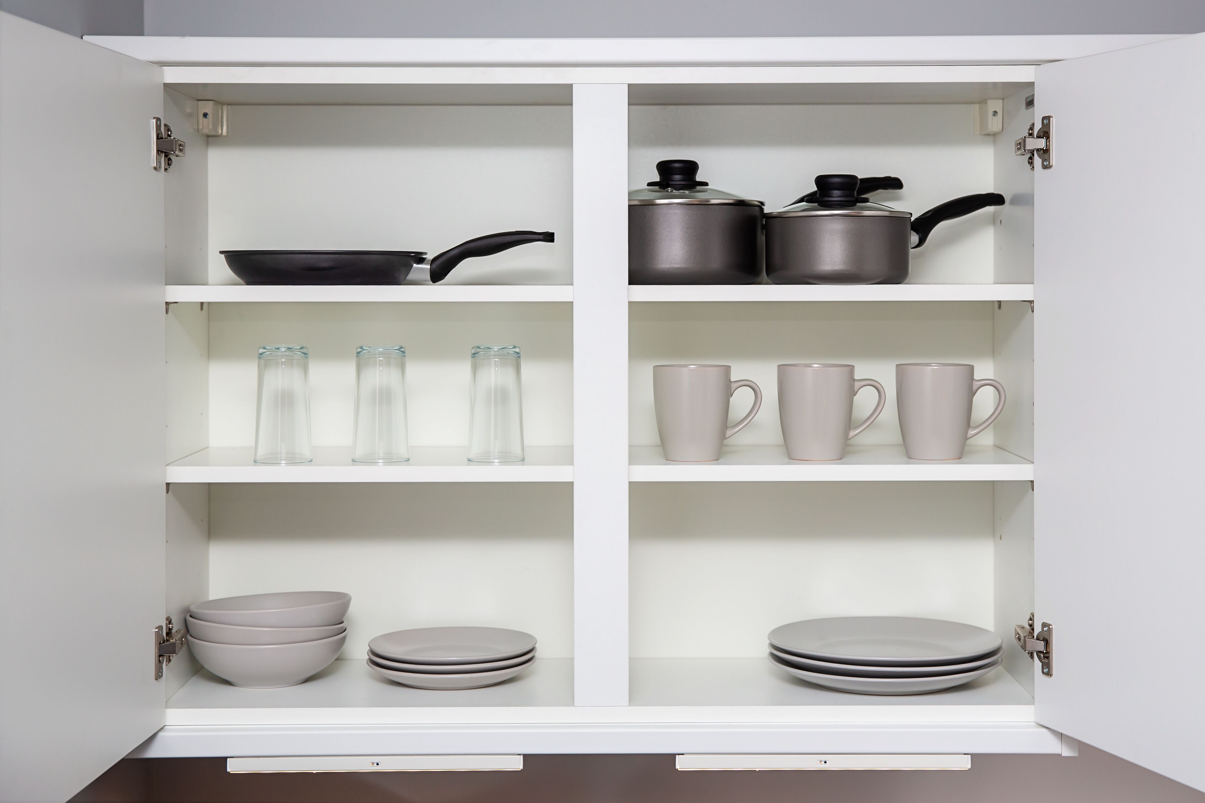 A white cabinet with shelves containing kitchenware, including plates, bowls, glasses, and cookware.