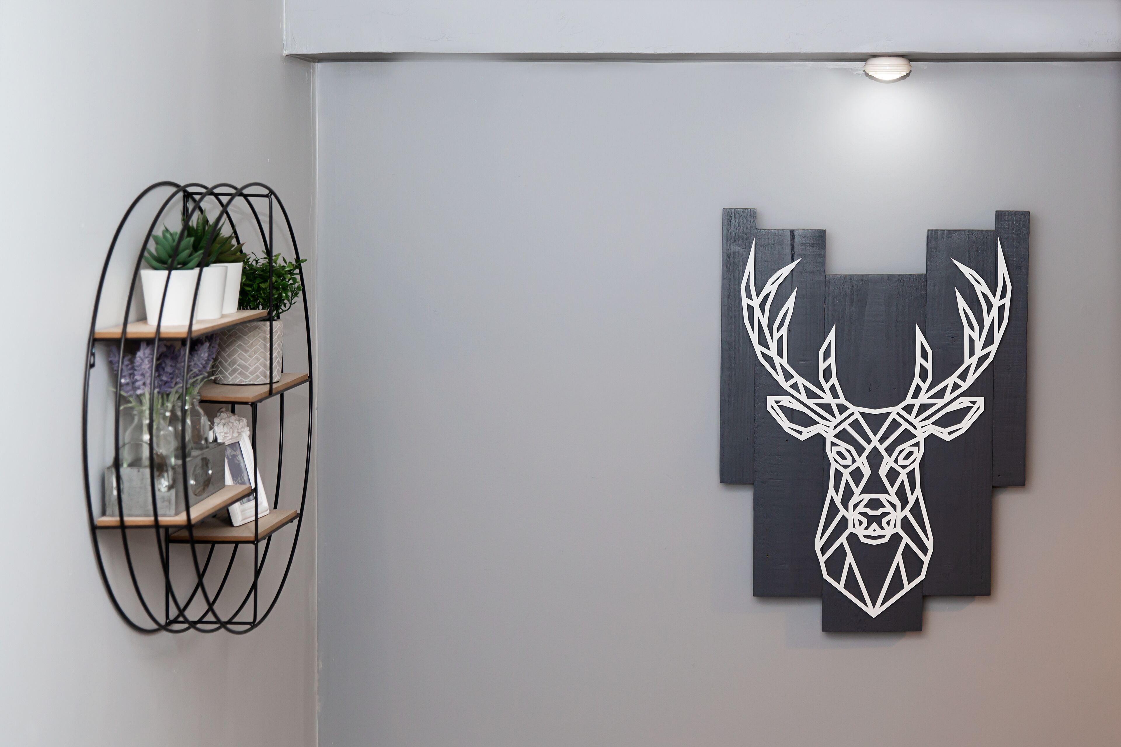 A wall with a geometric deer head artwork and a metal plant shelf.