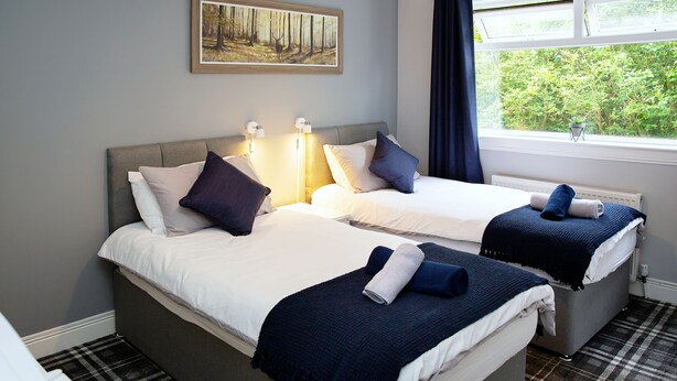 A room with two beds, a painting on the wall, and a window with a view of greenery. - St Andrews Guest House (Irvine)