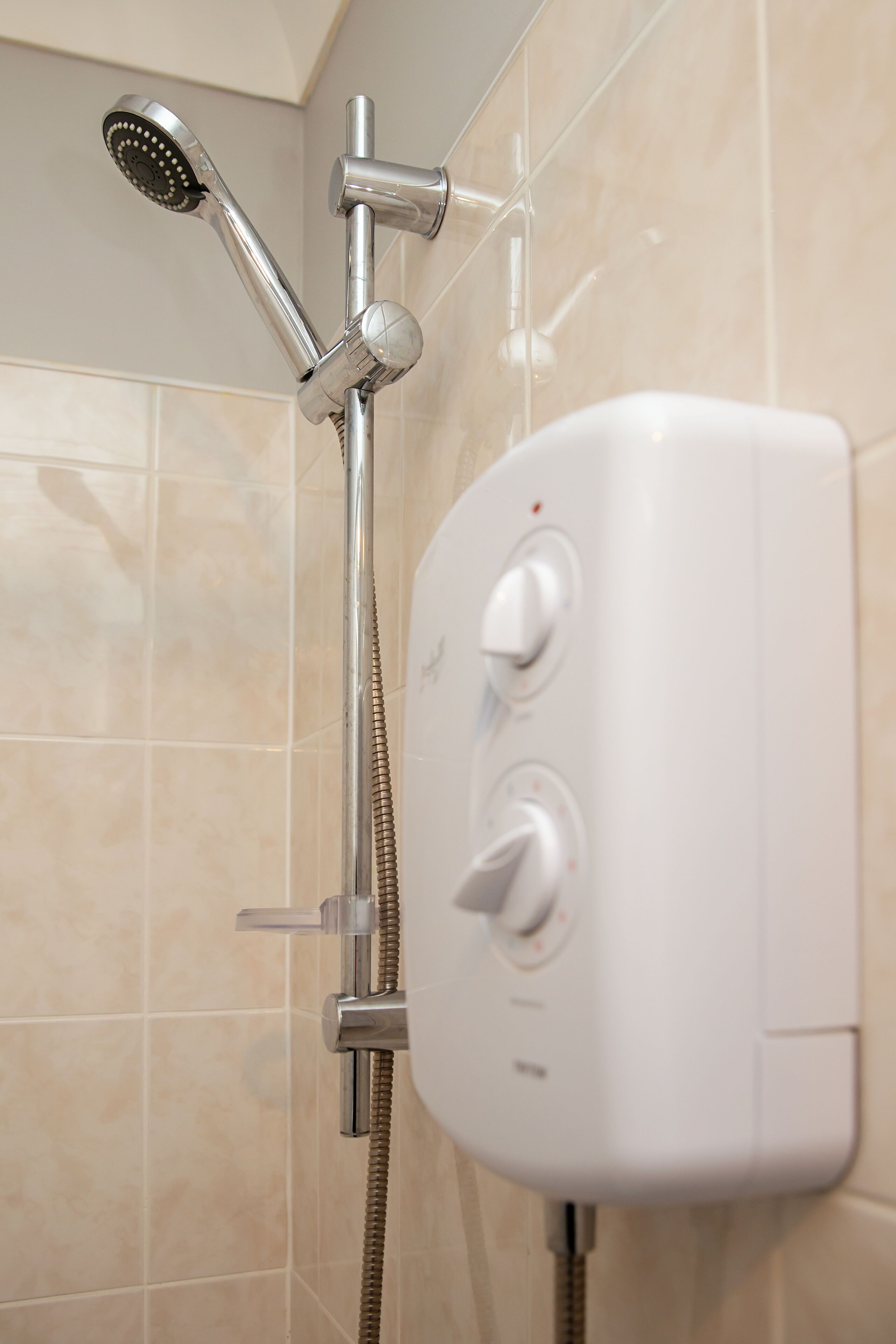 A shower with a handheld showerhead and a wall-mounted control panel.