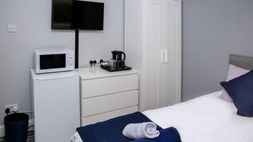 Habitación de hotel con una cama, un televisor montado en la pared, microondas, cafetera y armario.