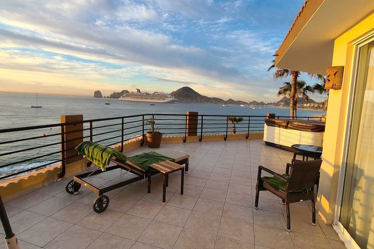 Un balcón con vistas al mar, una silla de descanso, una mesita y una planta en maceta.