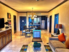 A spacious living room with a television, sofa, and coffee table. A kitchen is visible in the background with a dining area. - The Islands of Loreto Resort and Spa (Loreto)