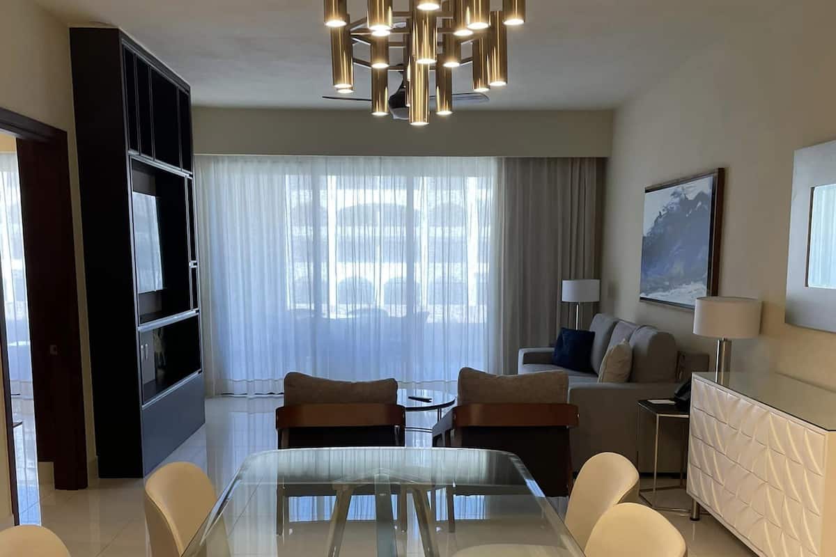 Una sala de estar moderna con una mesa de comedor de vidrio, un sofá, un televisor y una araña.