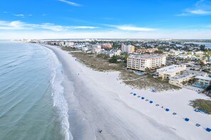 A coastal cityscape with a wide sandy beach, beachfront buildings, and a clear blue sky.