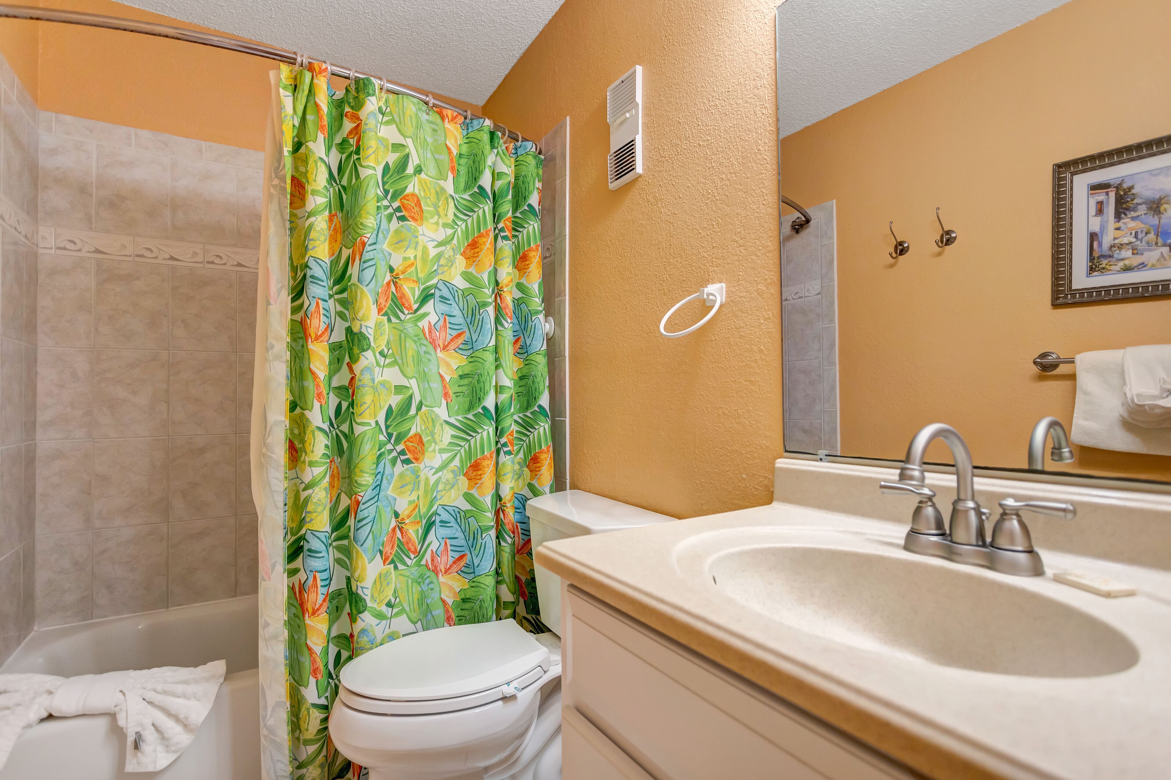 Un bagno con doccia, WC, lavabo e uno specchio con una cornice e un'immagine.
