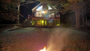 Une cabane avec un foyer à l’extérieur, entourée d’arbres.